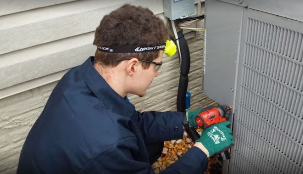 A technician works on an air conditioning unit outdoors