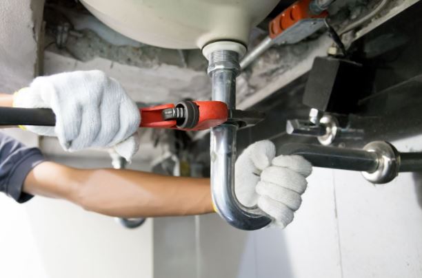 Technician plumber using a wrench to repair a water pipe under the sink. Concept of maintenance, fix water plumbing leaks, replace the kitchen sink drain, cleaning clogged pipes is dirty or rusty.