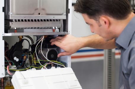 HVAC technician working on the internal components of a furnace, inspecting and adjusting wires and parts.