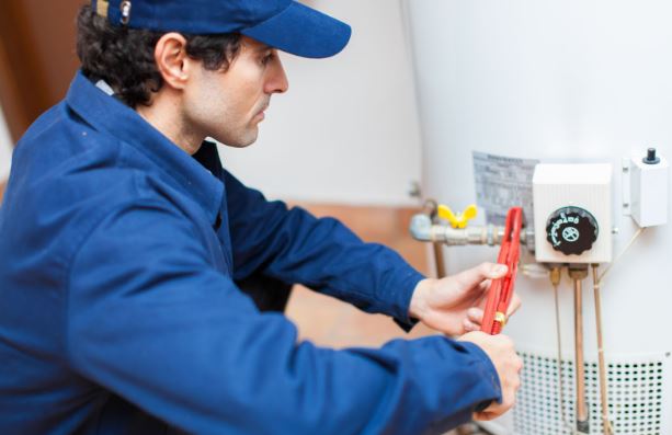 Water heater services man in Chesapeake, VA, fixing a residential water heater pipe with tools.